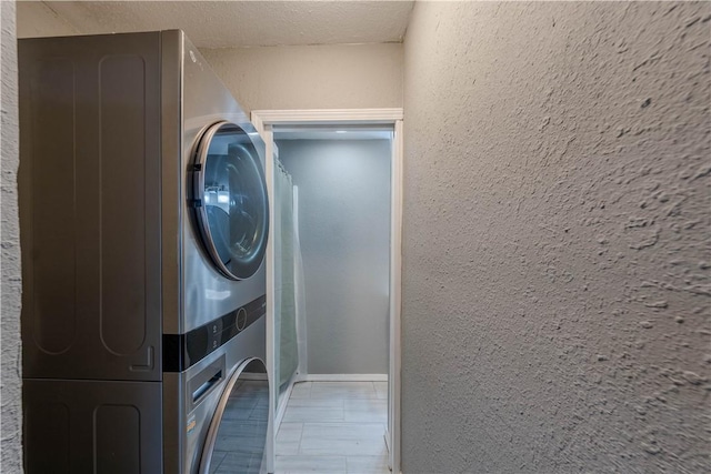 washroom featuring laundry area, baseboards, a textured wall, and stacked washing maching and dryer