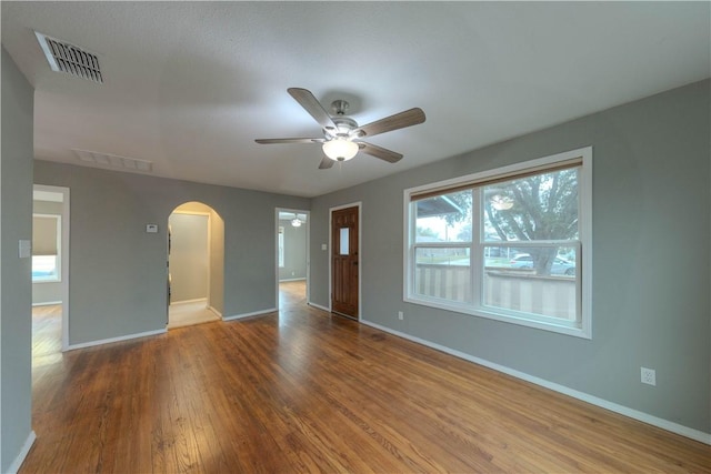 spare room with baseboards, visible vents, arched walkways, and wood finished floors