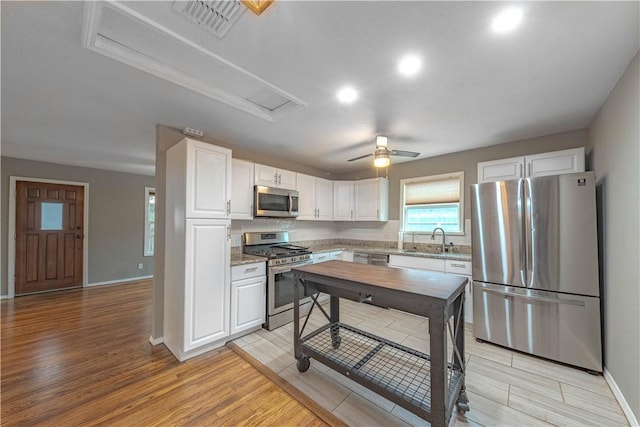 kitchen featuring visible vents, white cabinets, light wood-style flooring, appliances with stainless steel finishes, and a sink