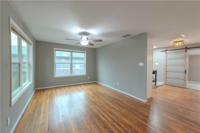 empty room with visible vents, a barn door, ceiling fan, wood finished floors, and baseboards