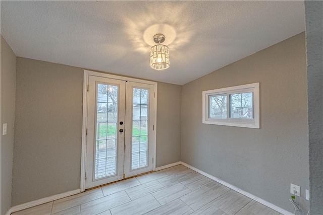 doorway featuring french doors, a textured wall, vaulted ceiling, a textured ceiling, and baseboards