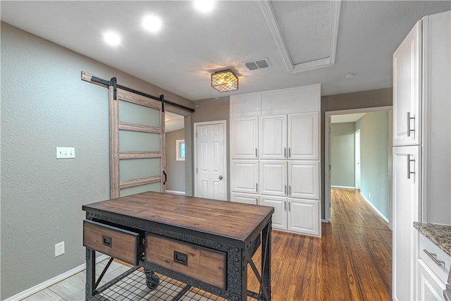 office featuring a barn door, visible vents, baseboards, a textured wall, and dark wood-style floors