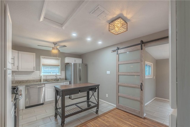 kitchen with a barn door, light stone countertops, wood tiled floor, stainless steel appliances, and white cabinetry