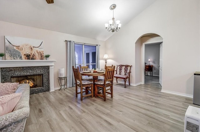 dining area featuring arched walkways, light wood-style floors, a chandelier, baseboards, and a tiled fireplace