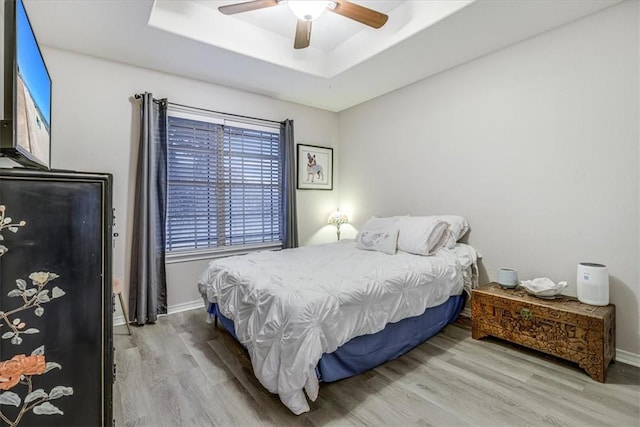 bedroom with wood finished floors, a tray ceiling, baseboards, and a ceiling fan