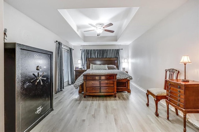 bedroom with wood finished floors, a tray ceiling, baseboards, and a ceiling fan