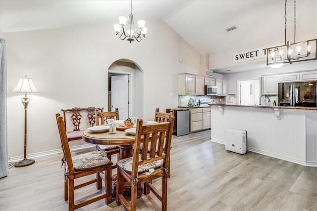 dining room featuring a chandelier, arched walkways, light wood-type flooring, high vaulted ceiling, and baseboards