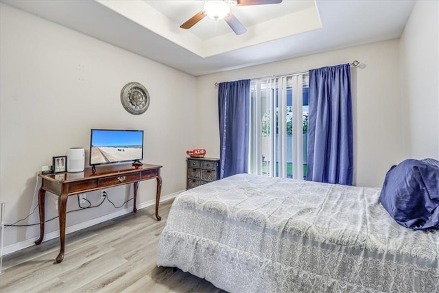 bedroom featuring wood finished floors, a tray ceiling, baseboards, and a ceiling fan