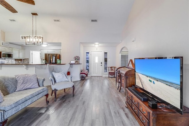 living area featuring high vaulted ceiling, light wood finished floors, arched walkways, a chandelier, and a ceiling fan