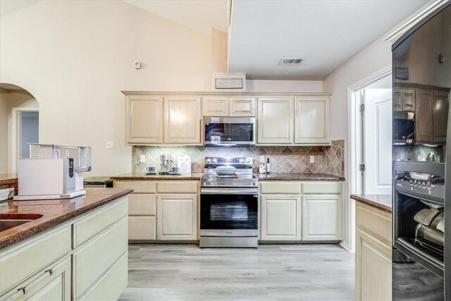 kitchen with stainless steel appliances, light wood finished floors, arched walkways, and backsplash