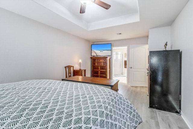 bedroom with light wood-style floors, a ceiling fan, and a raised ceiling