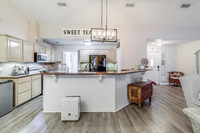 kitchen featuring appliances with stainless steel finishes, a breakfast bar, light wood finished floors, and a chandelier