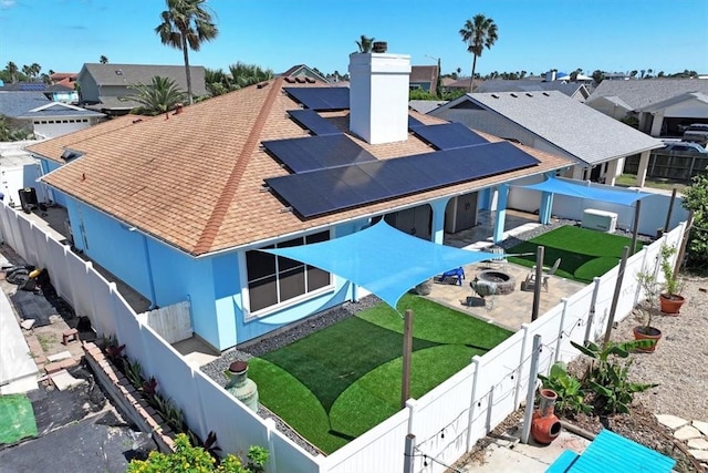 rear view of property with roof with shingles, a chimney, a patio area, solar panels, and a fire pit