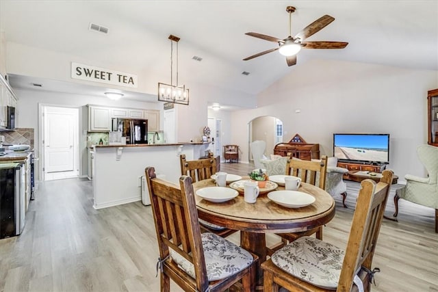 dining space featuring arched walkways, a ceiling fan, light wood finished floors, and vaulted ceiling