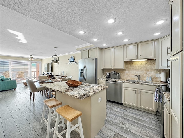 kitchen featuring sink, a center island, a textured ceiling, appliances with stainless steel finishes, and light wood-type flooring