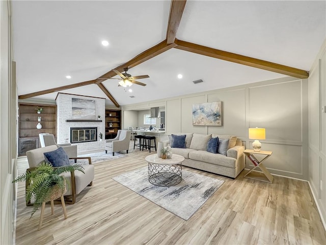 living area with lofted ceiling with beams, a brick fireplace, built in features, and a decorative wall