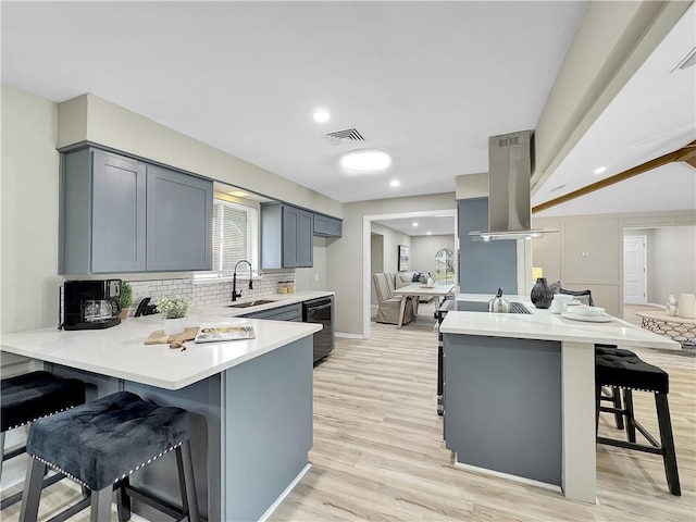 kitchen featuring a breakfast bar, a peninsula, island exhaust hood, light countertops, and a sink