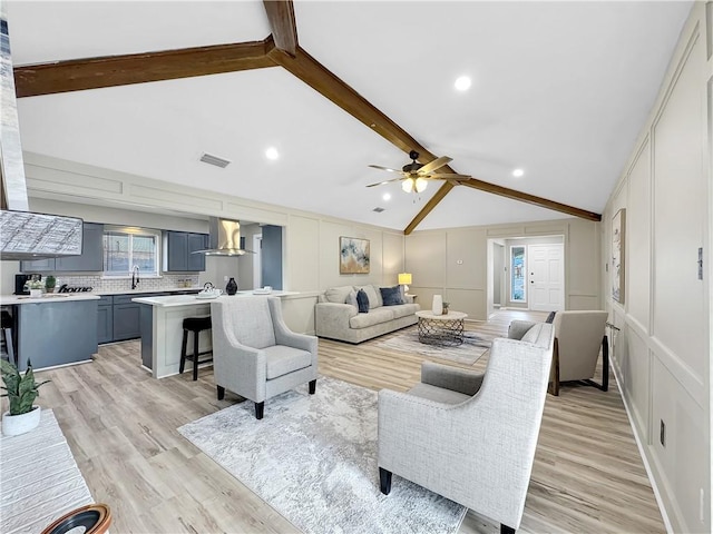 living room featuring light wood finished floors, visible vents, lofted ceiling with beams, a decorative wall, and a wealth of natural light