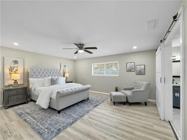 bedroom featuring light wood-type flooring, a barn door, visible vents, and baseboards