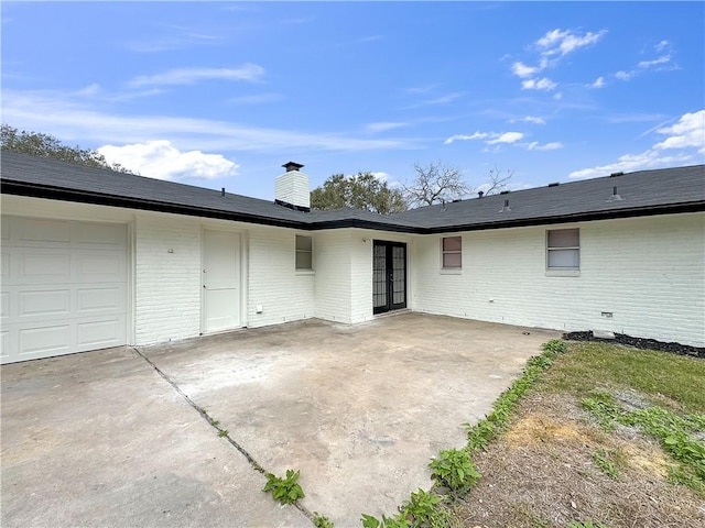 back of property with a chimney, crawl space, an attached garage, french doors, and brick siding