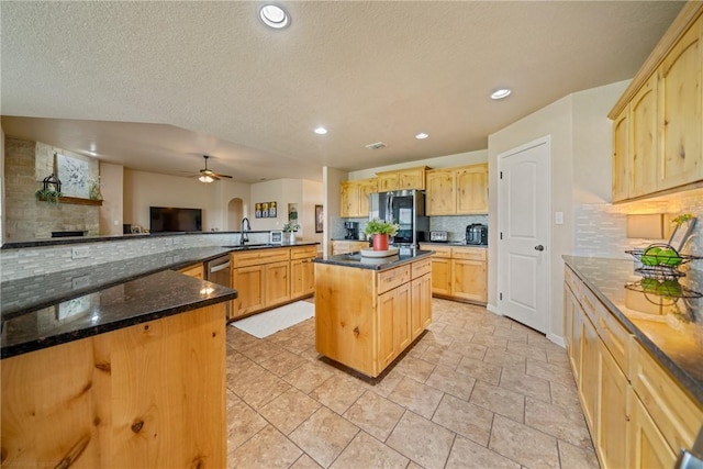 kitchen featuring stainless steel appliances, light brown cabinetry, a kitchen island, and dark stone counters