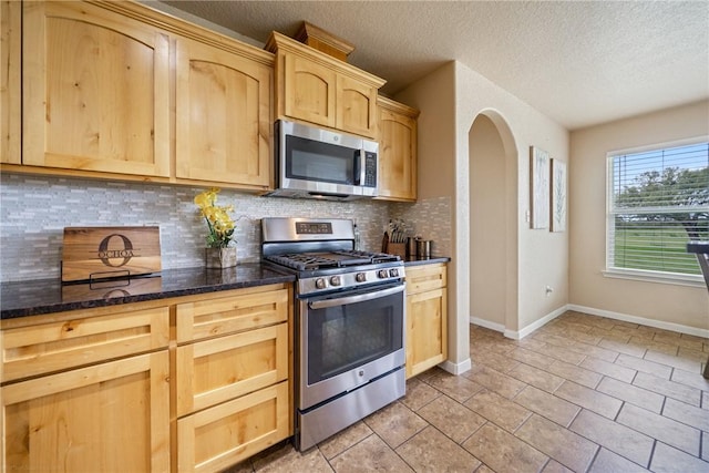 kitchen featuring dark stone countertops, stainless steel appliances, tasteful backsplash, light tile patterned flooring, and light brown cabinets