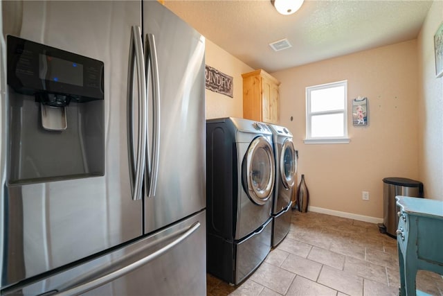 laundry area featuring cabinets, light tile patterned flooring, a textured ceiling, and washer and clothes dryer