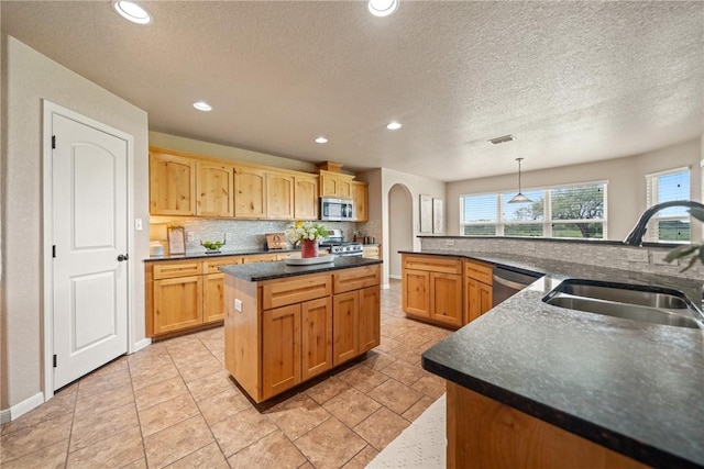 kitchen with pendant lighting, sink, backsplash, stainless steel appliances, and a kitchen island