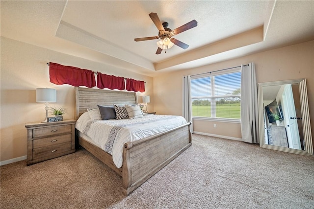 bedroom featuring light carpet, ceiling fan, a tray ceiling, and a textured ceiling