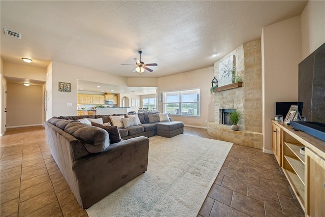 living room featuring ceiling fan, a fireplace, and a textured ceiling