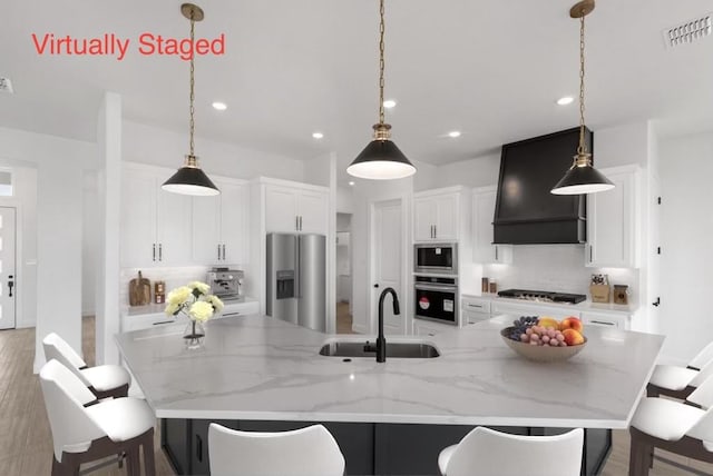 kitchen with premium range hood, a kitchen bar, visible vents, a sink, and stainless steel appliances