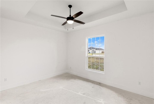 unfurnished room featuring ceiling fan, unfinished concrete floors, a raised ceiling, and baseboards