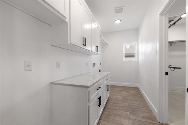 laundry room featuring visible vents, baseboards, cabinet space, electric dryer hookup, and light wood-style floors