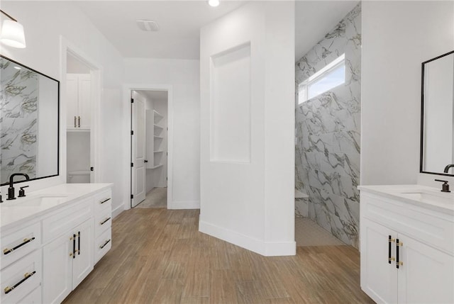 bathroom with a sink, a marble finish shower, two vanities, and wood finished floors