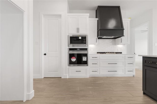 kitchen with decorative backsplash, custom exhaust hood, appliances with stainless steel finishes, and white cabinetry