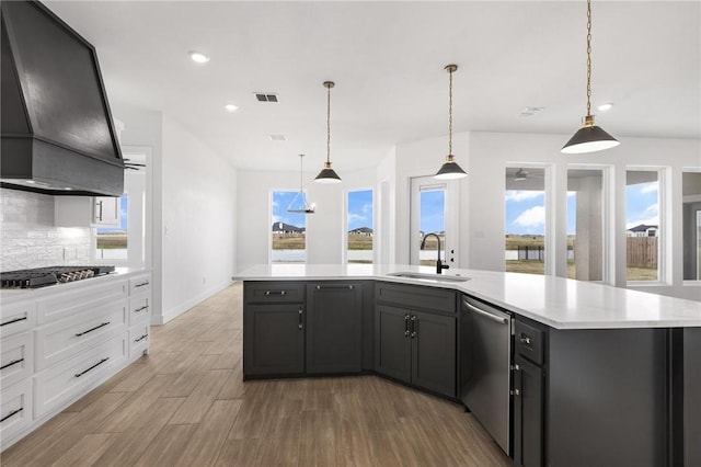 kitchen with a sink, wall chimney range hood, gas cooktop, stainless steel dishwasher, and light countertops