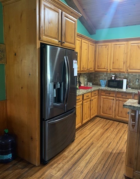 kitchen featuring black appliances, tasteful backsplash, light stone counters, light hardwood / wood-style floors, and beamed ceiling