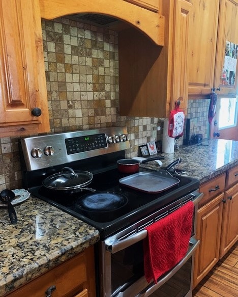 kitchen with dark stone counters, backsplash, stainless steel range with electric stovetop, and light hardwood / wood-style floors