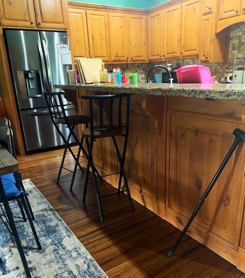 kitchen with stainless steel refrigerator with ice dispenser, dark wood-type flooring, light stone counters, and backsplash