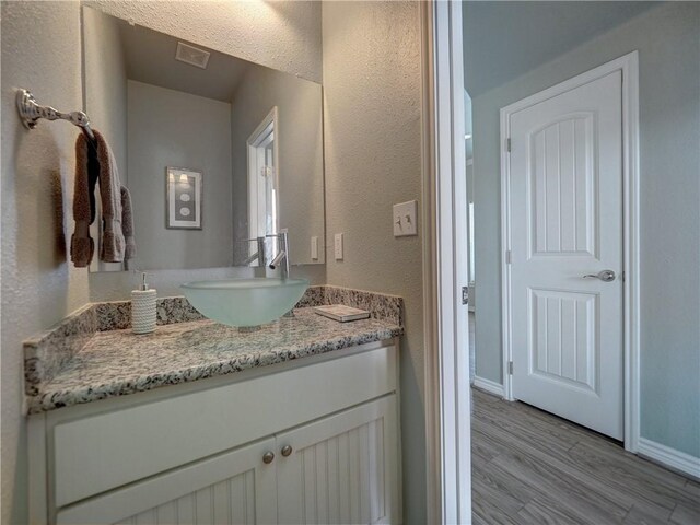 bathroom featuring wood finished floors, vanity, baseboards, and a textured wall
