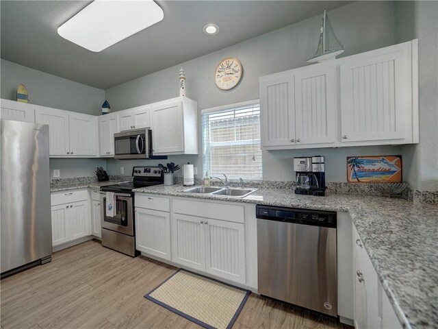 kitchen featuring stainless steel appliances, a sink, white cabinets, light wood-style flooring, and recessed lighting