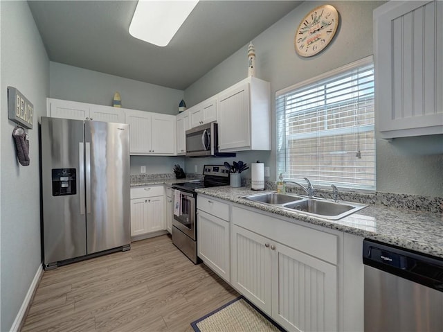 kitchen with stainless steel appliances, a sink, white cabinetry, light wood-type flooring, and baseboards