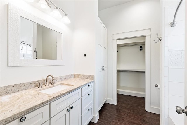 full bathroom with baseboards, a shower, a walk in closet, vanity, and wood finished floors