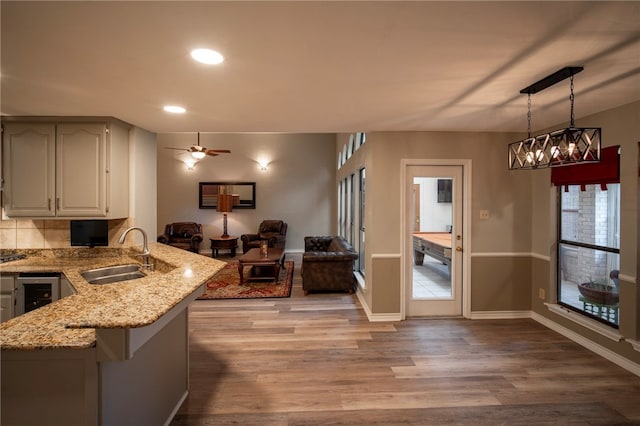 kitchen with kitchen peninsula, sink, ceiling fan, light wood-type flooring, and decorative light fixtures