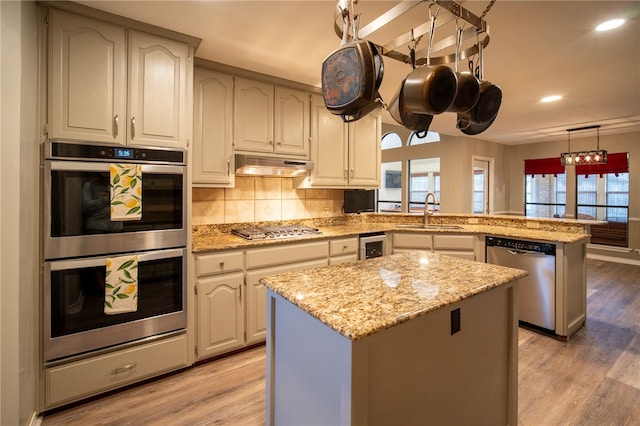 kitchen featuring stainless steel appliances, light hardwood / wood-style floors, a center island, kitchen peninsula, and sink