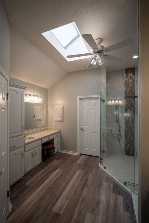 bathroom with hardwood / wood-style flooring, vanity, ceiling fan, vaulted ceiling with skylight, and walk in shower