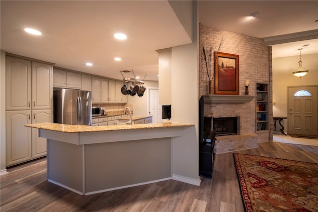 kitchen with kitchen peninsula, appliances with stainless steel finishes, decorative light fixtures, a fireplace, and dark wood-type flooring