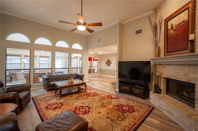 living room featuring a brick fireplace, light hardwood / wood-style floors, a towering ceiling, ceiling fan, and crown molding