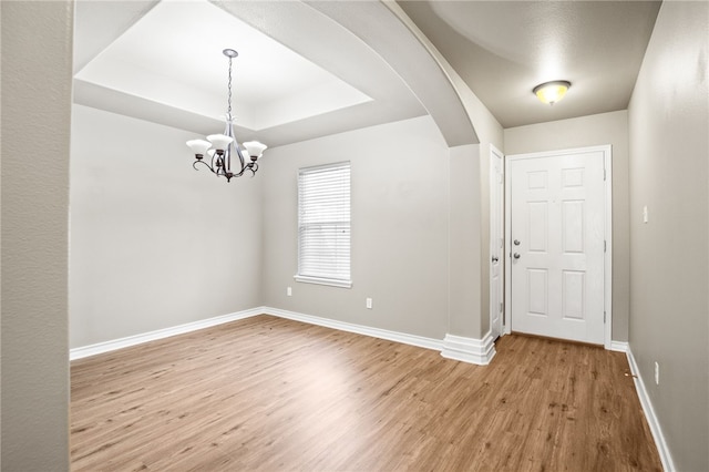 empty room with light wood-type flooring, a raised ceiling, and an inviting chandelier