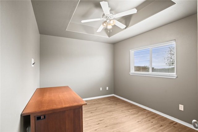 unfurnished office featuring light hardwood / wood-style flooring, ceiling fan, and a tray ceiling